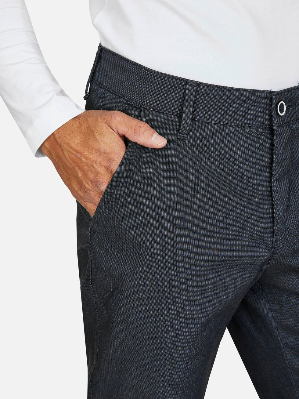 Nahaufnahme einer dunkelgrauen GARVEY 6910 Flat Front-Hose mit elastischem Komfortbund, Hemdstopper, Baumwoll-Mikrostruktur in Woll-Optik, normale Leibhöhe, schmaler Beinverlauf und sichtbarer Tasche, getragen von einer Person in weißem Hemd.