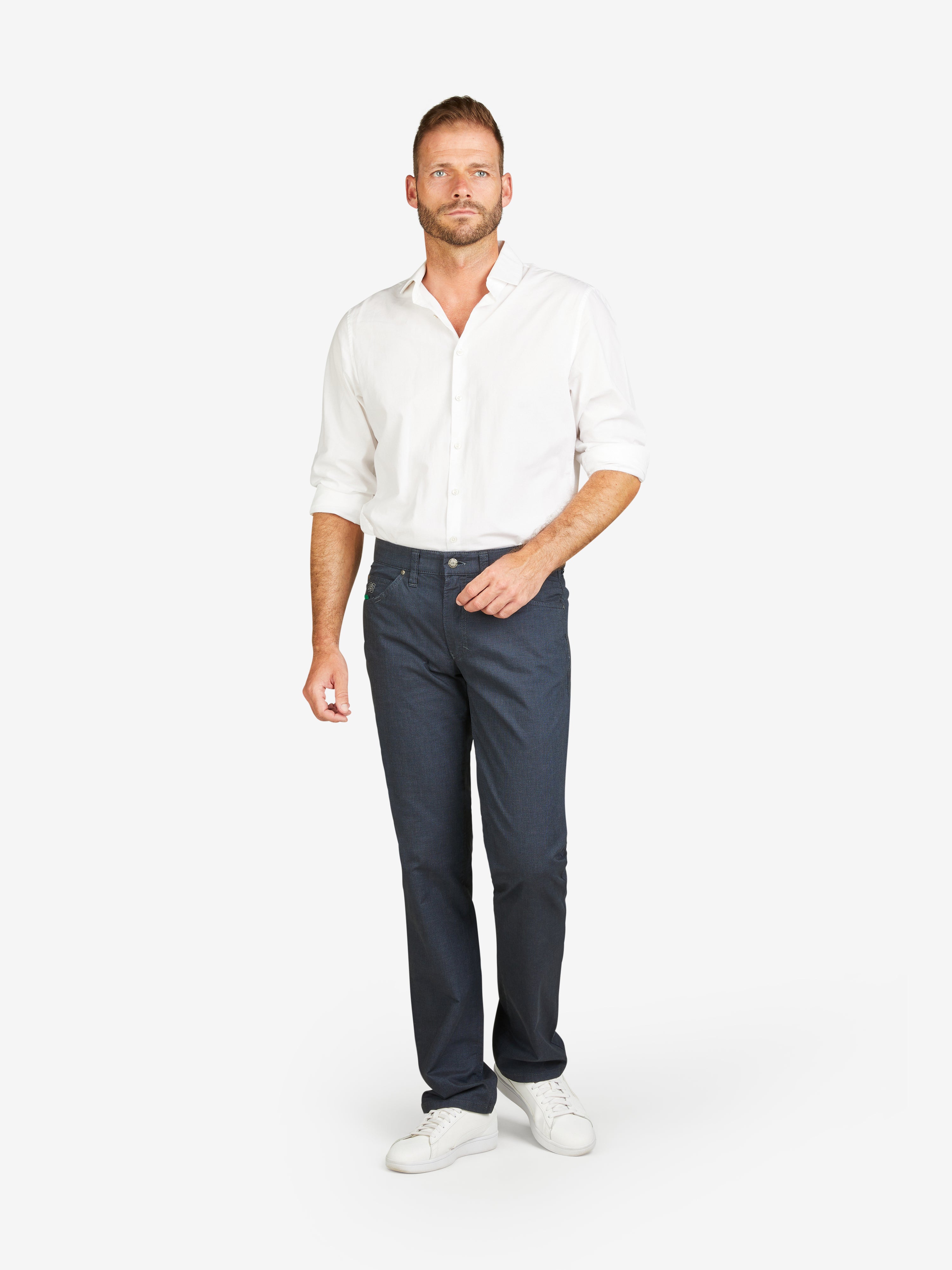 Mann trägt eine dunkelblaue HENRY 6910 5-Pocket Baumwollhose mit Stretch, Komfortbund, Mobile Pocket, Münztasche mit Kontrast-Patch, in Woll-Optik, kombiniert mit weißem Hemd und weißen Sneakers.
