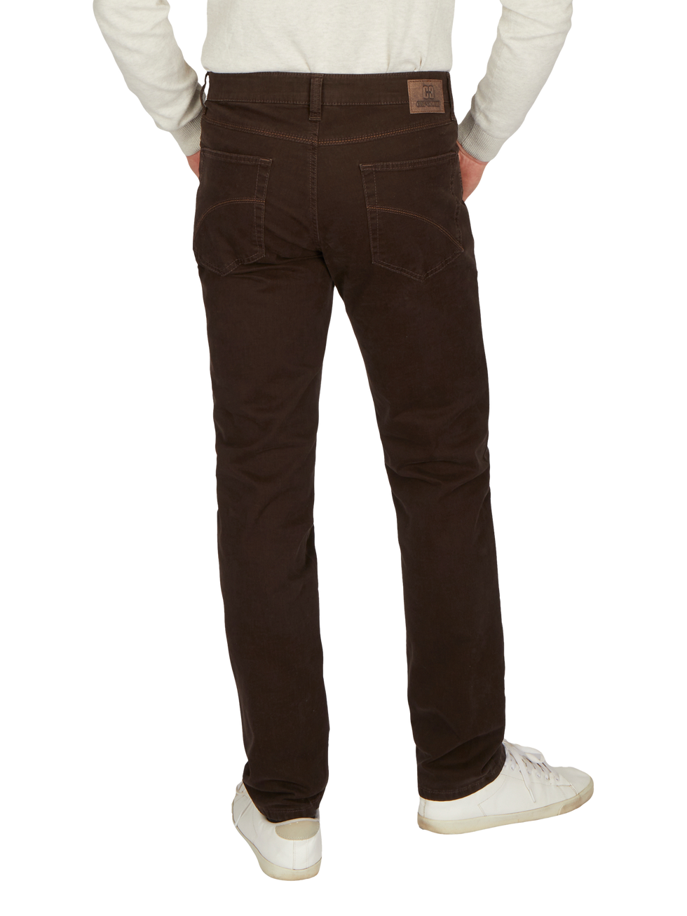 Blick auf eine Person, die schwarze Jeans trägt, mit sichtbaren Rückentaschen, Gürtelschlaufen und einem kleinen Lederetikett am Bund. Die Person trägt ein hellgraues Oberteil und weiße Schuhe.