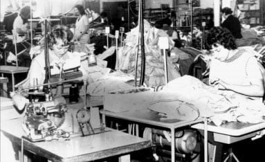 Schwarz-Weiß-Bild einer Näherei mit mehreren Frauen, die an Stichen und Nähmaschinen in einer Arbeitsumgebung arbeiten, um Kleidung oder Stoffe herzustellen.