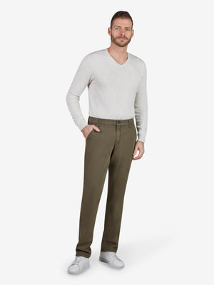 Mann trägt eine grüne GARVEY 8070 Flat Front-Hose aus bi-elastischer Baumwolle mit softem Griff, elastischem Komfortbund, Hemdstopper, Münztasche, normaler Leibhöhe, schlanker Beinform, kombiniert mit weißem Pullover und weißen Sneakers.
