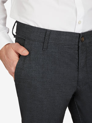 Nahaufnahme einer schwarzen Flat Front-Hose von Club of Comfort, mit elastischem Komfortbund und Hemdstopper, aus Baumwoll-Struktur-Mischgewebe mit Woll-Optik, normaler Leibhöhe, schmaler Beinverlauf, perfekt für Herbst/Winter, mit sichtbarem Gürtel und Knopf.