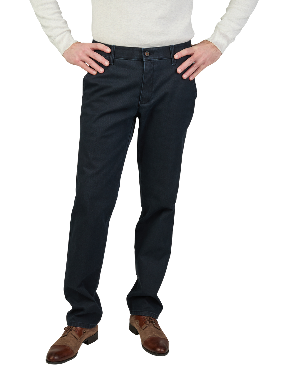 Ein Mann trägt dunkle Jeanshosen, ein helles langärmeliges Hemd und braune Lederschuhe, steht mit den Händen in den Hüften.