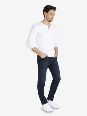 Mann trägt dunkelblaue, washed HENRY 7054 6-Pocket Jeanshose aus superelastischem Bi-Stretch-Denim mit Komfortbund, Hemdstopper und separater Mobile Pocket. Figurbetonter Regular Fit, normale Leibhöhe, flexible Elastizität, in weißem Hemd und weißen Sneakers.