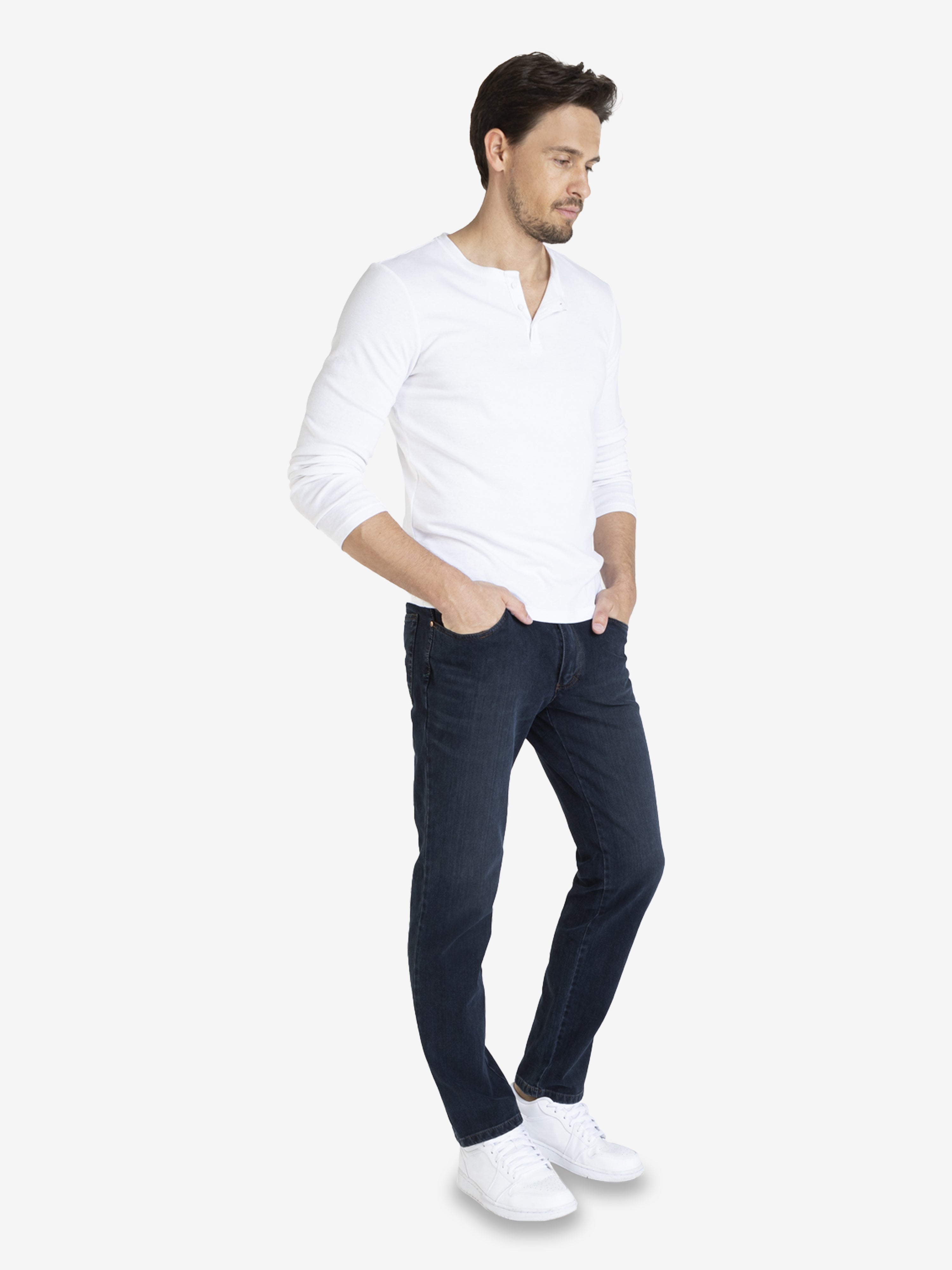 Mann trägt dunkelblaue, washed HENRY 7054 6-Pocket Jeanshose aus superelastischem Bi-Stretch-Denim mit Komfortbund, Hemdstopper und separater Mobile Pocket. Figurbetonter Regular Fit, normale Leibhöhe, flexible Elastizität, in weißem Hemd und weißen Sneakers.