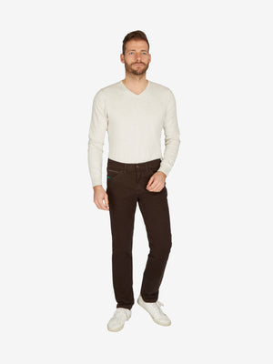 Mann trägt braune HENRY 7612 6-Pocket Baumwollhose von Club of Comfort mit elastischem Doppelstoffbund, Hemdstopper und separater Mobile Pocket in der rechten Vordertasche, kombiniert mit einem weißen Pullover und weißen Sneakers.